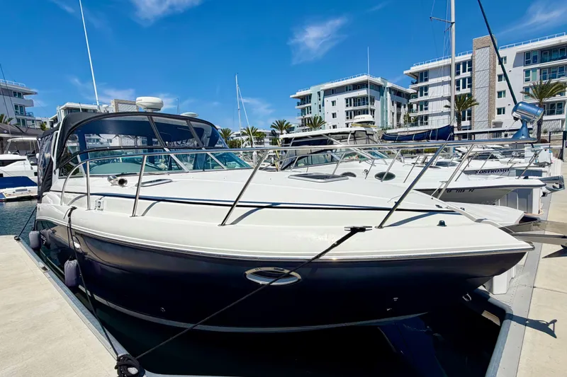 The Image of 2006 Rinker 320 Express Cruiser docked at a marina under a clear blue sky. - 0