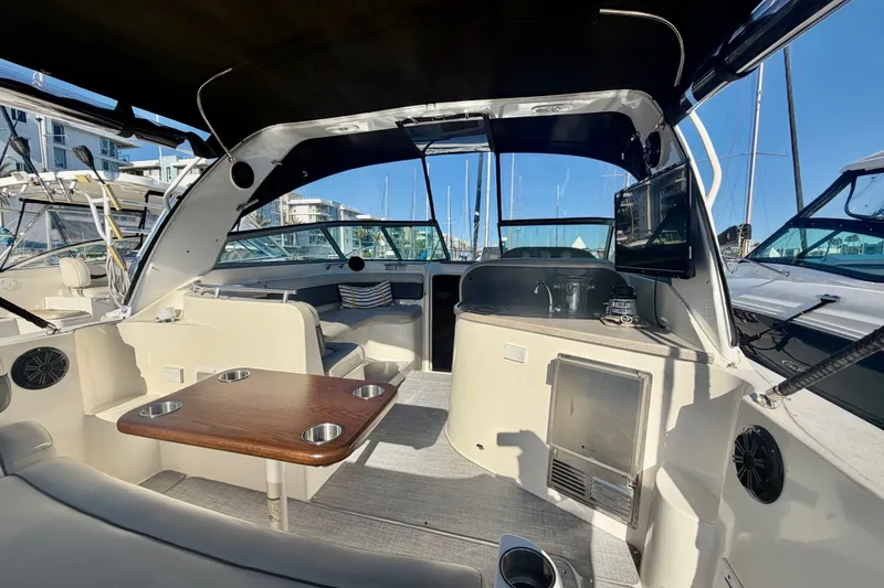 Slide: The Image of 2006 Rinker 320 Express Cruiser interior with seating, table, and kitchenette in marina setting. - 19