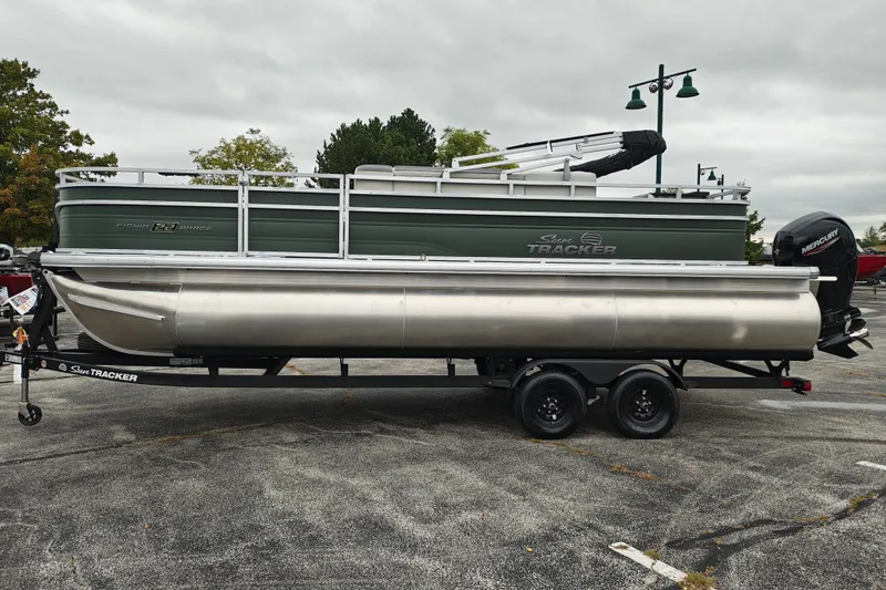 The Image of 2027 Sun Tracker Fishin' Barge 22 XP3 pontoon boat on trailer, parked outdoors. - 1
