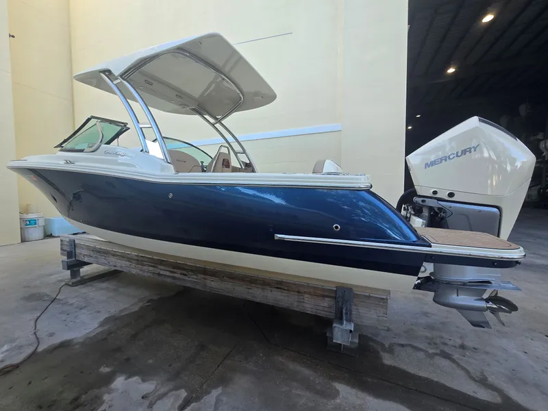 The Image of 2023 Chris-Craft Calypso 24 with a blue hull and Mercury outboard motor, on a wooden stand. - 0