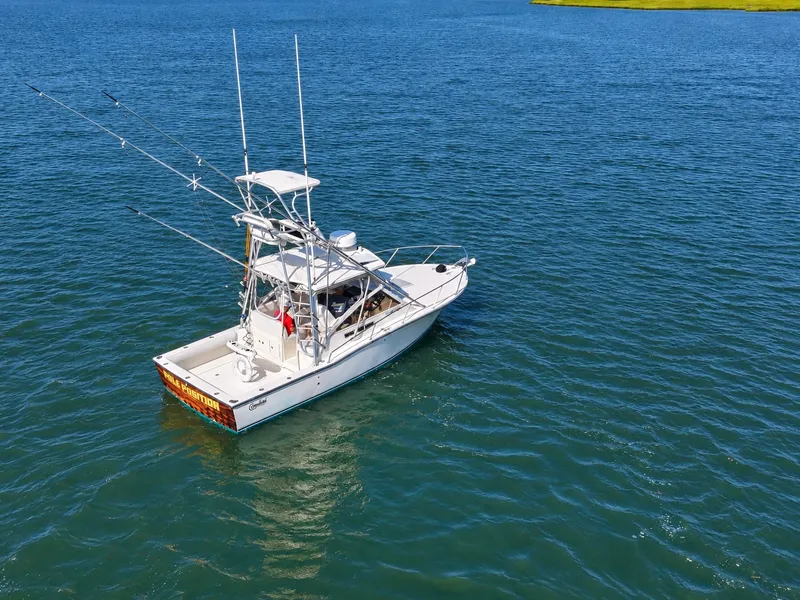 Slide: The Image of A 2005 Carolina Classic 28 Express on calm water with fishing rods and an elevated helm. - 1