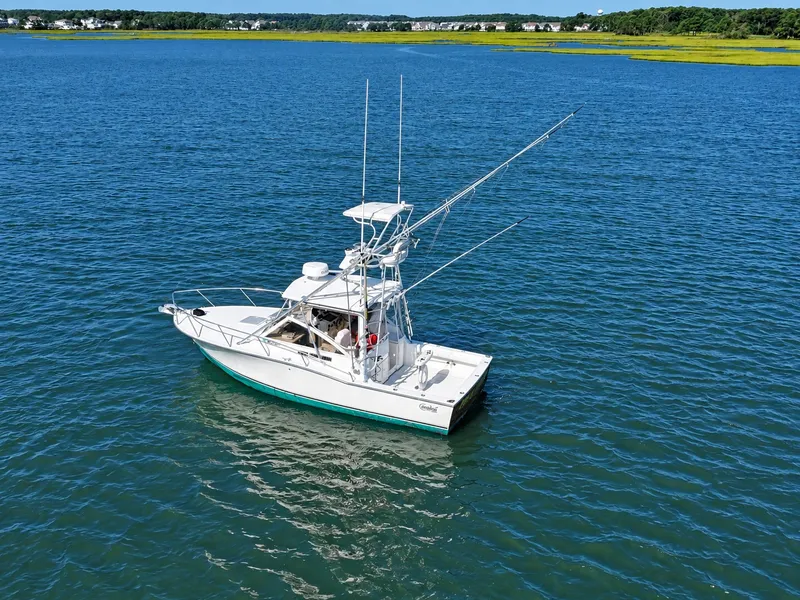 Slide: The Image of A 2005 Carolina Classic 28 Express boat on calm water with a green shoreline in the background. - 2
