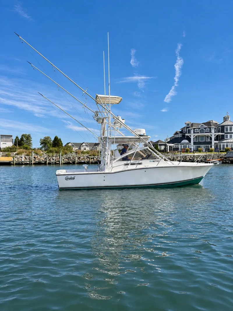Slide: The Image of A 2005 Carolina Classic 28 Express boat on calm water with a coastal backdrop. - 4