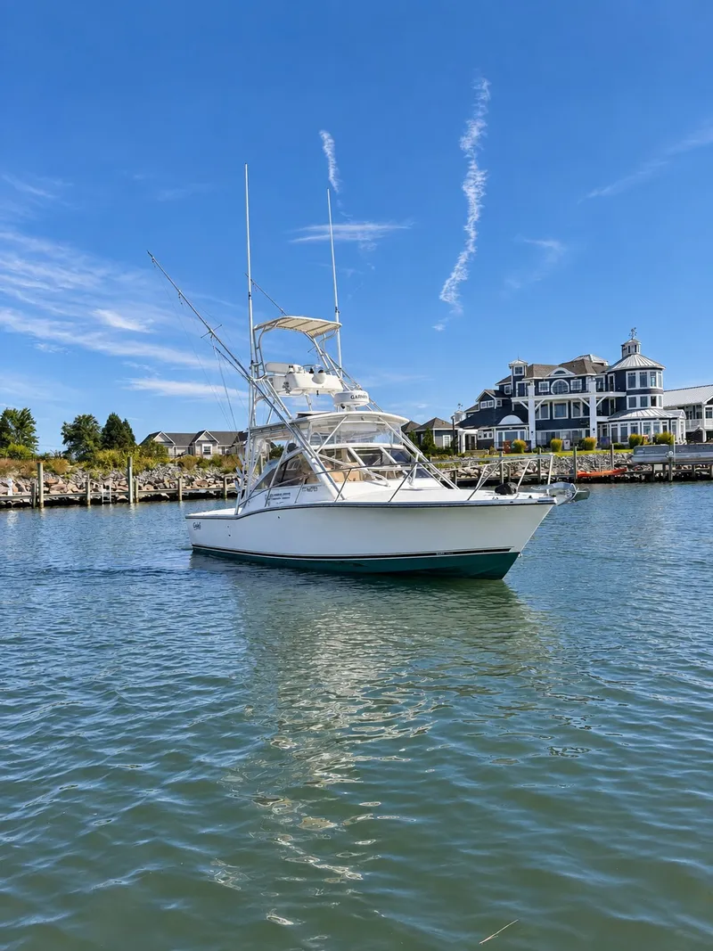 Slide: The Image of A 2005 Carolina Classic 28 Express boat on calm water in front of a large building. - 5