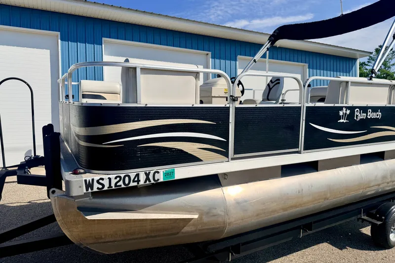 Slide: The Image of 2011 Palm Beach Sport Fish 1623 SE pontoon boat on trailer, parked near blue building. - 13