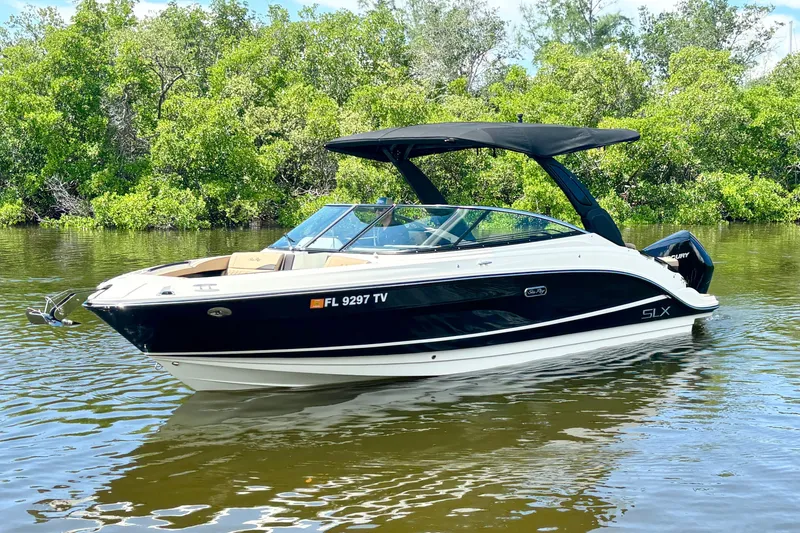 Slide: The Image of 2023 Sea Ray SLX 260 Outboard boat on calm water, surrounded by lush greenery. - 5