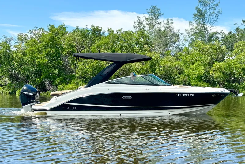 Slide: The Image of 2023 Sea Ray SLX 260 Outboard boat cruising on a calm river with lush greenery. - 1