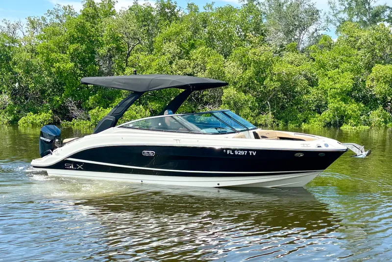 The Image of 2023 Sea Ray SLX 260 Outboard boat cruising on a calm river with lush greenery. - 0