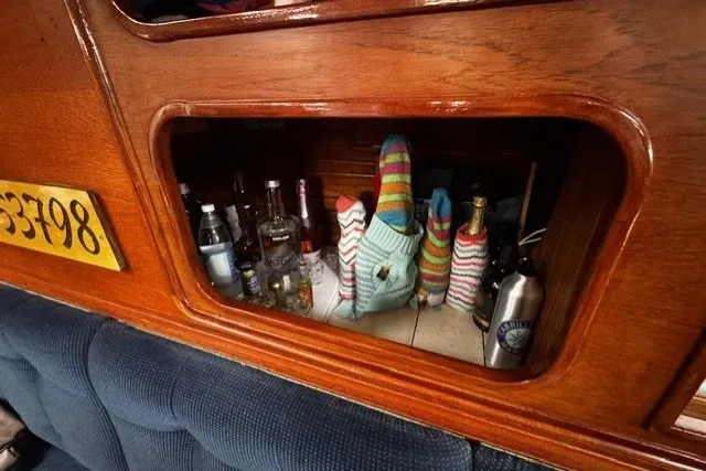 Slide: The Image of Wooden cabinet on 1973 C&C 48 yacht with assorted bottles and colorful knit covers. - 19