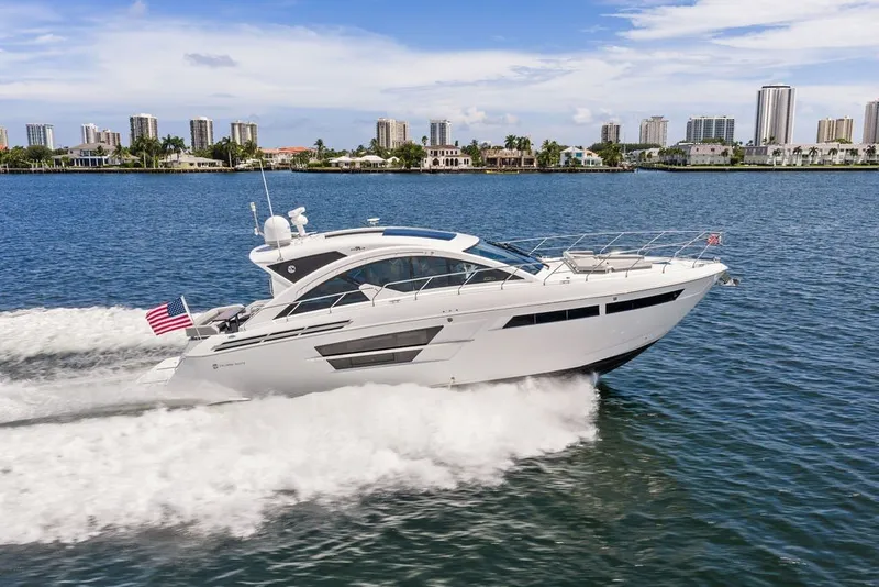 The Image of 2022 Cruisers Yachts 54 Cantius cruising on water with city skyline backdrop. - 0