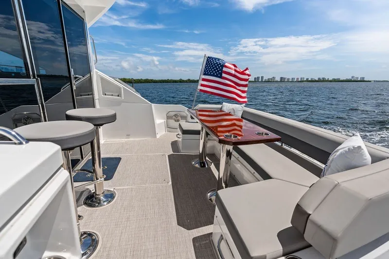 Slide: The Image of 2022 Cruisers Yachts 54 Cantius deck with seating, table, and American flag on open water. - 33