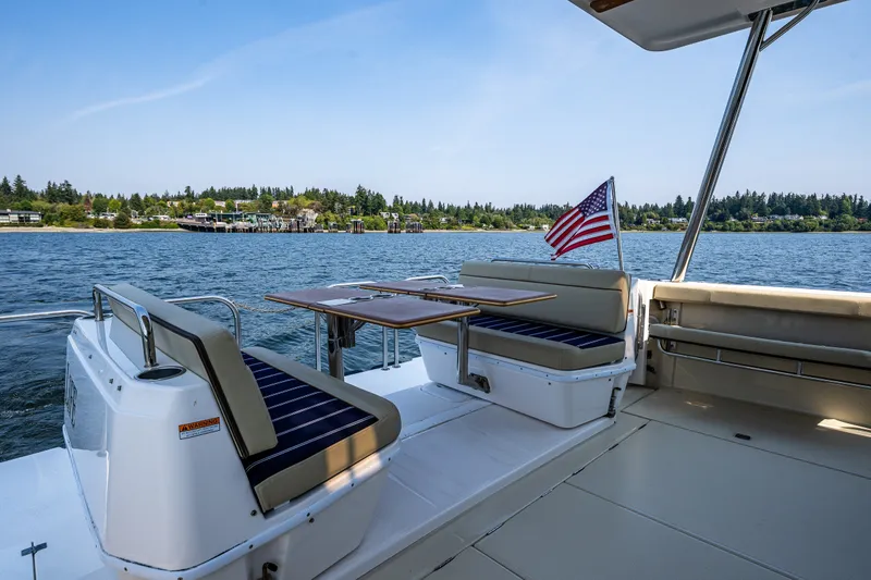 Slide: The Image of 2020 Ranger Tugs R-41 CB boat deck with seating, table, and American flag on a scenic lake. - 12