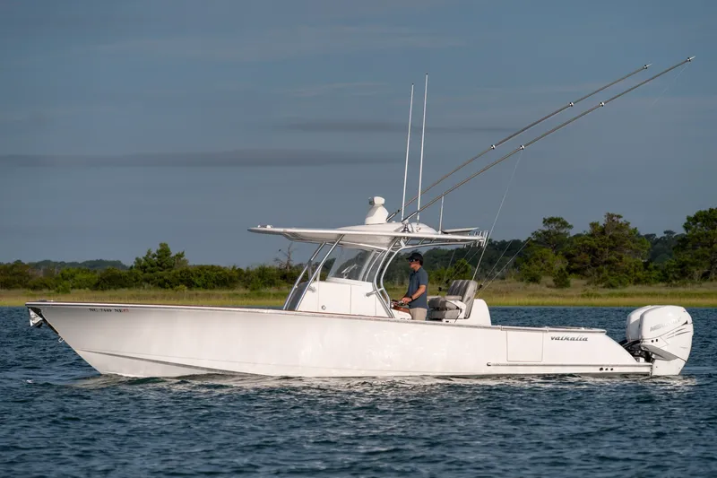 Slide: The Image of 2021 Valhalla V-33 boat cruising on calm water with trees in the background. - 2