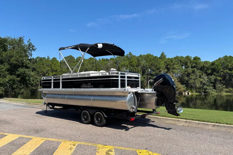 Slide: The Image of 2027 Sun Tracker Fishin' Barge 22 XP3 pontoon boat on trailer by a lake. - 110