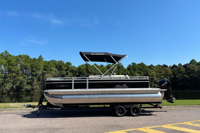 The Image of 2027 Sun Tracker Fishin' Barge 22 XP3 pontoon boat on trailer by a lake. - 0