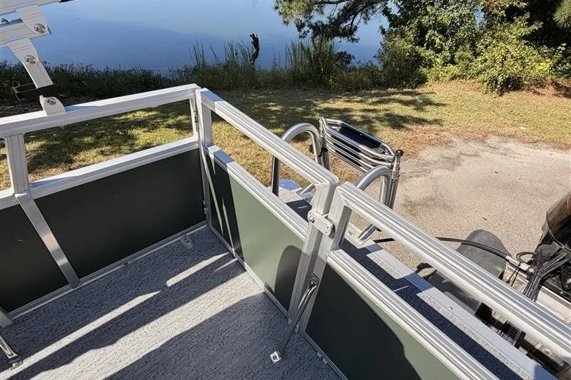 Slide: The Image of 2027 Sun Tracker Bass Buggy 16 XL Select pontoon boat near a serene lakeside. - 15