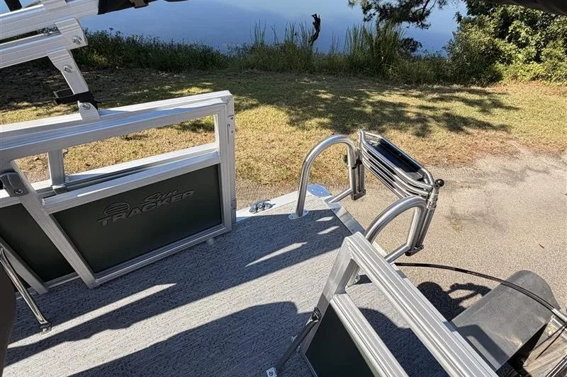 Slide: The Image of 2027 Sun Tracker Bass Buggy 16 XL Select pontoon boat near a serene lakeside. - 16