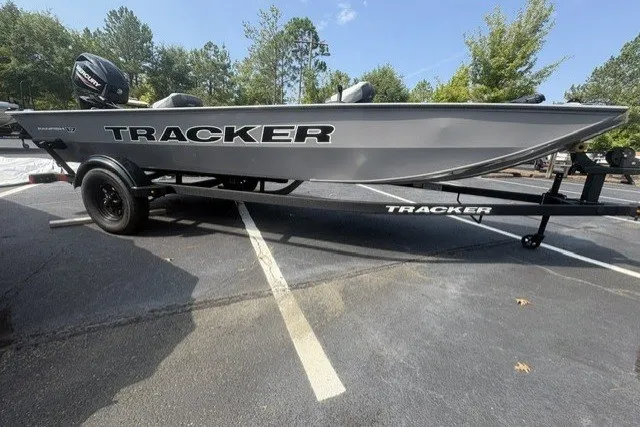 The Image of 2027 Tracker Panfish 17 boat on trailer in parking lot, surrounded by trees. - 0