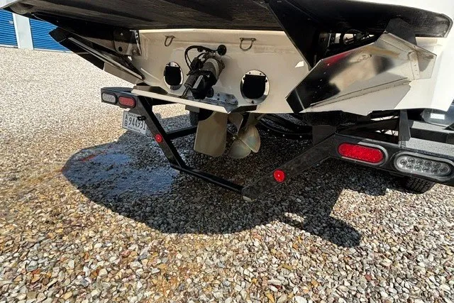 Slide: The Image of 2022 MasterCraft NXT22 boat rear view showing propeller and trailer on gravel. - 2