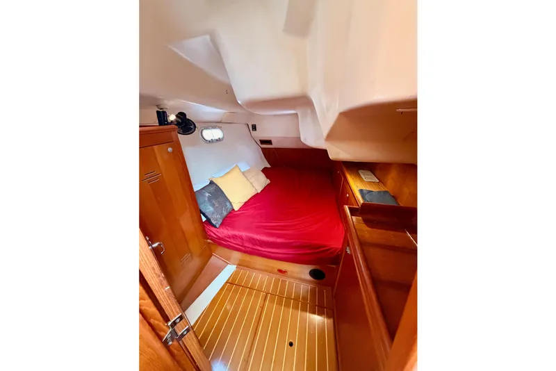 Slide: The Image of The cabin of a 2000 Hunter 460 with a cozy bed, wooden floor, and storage space. - 25