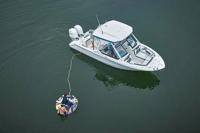 Slide: The Image of 2027 Cobia 250 Dual Console boat towing a colorful inflatable on calm water. - 14