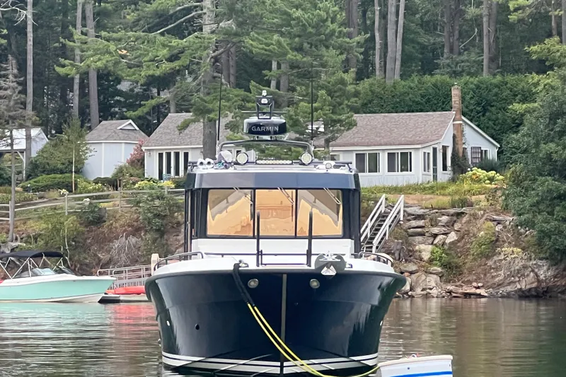 Slide: The Image of 2024 Targa 32 boat docked near lakeside cabin with lush greenery. - 2