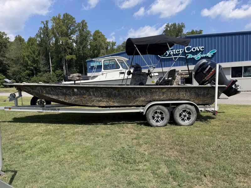 The Image of A 2023 War Eagle 2170 Blackhawk boat on a trailer, featuring a black canopy and outboard motor. - 1