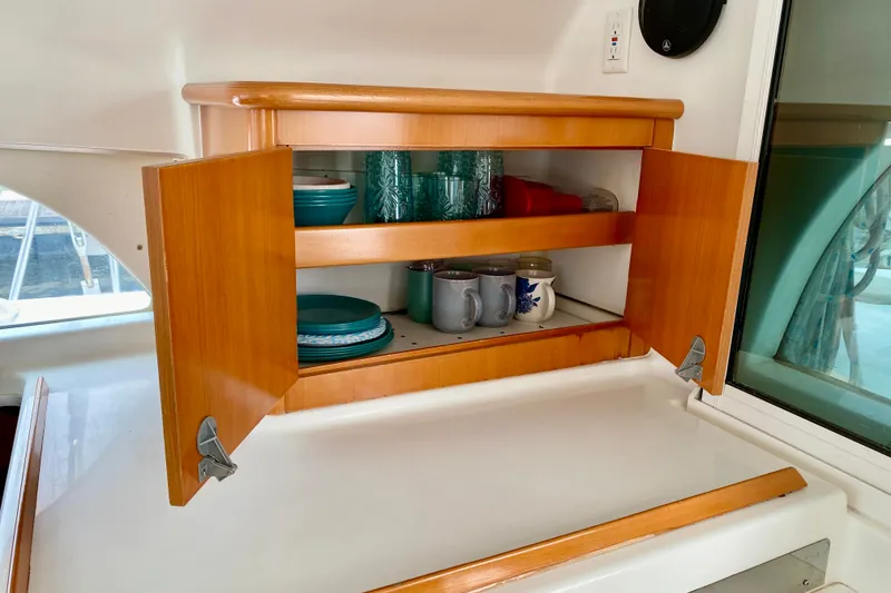 Slide: The Image of Wooden cabinet with open doors displaying dishes and mugs inside a 2005 Lagoon 380 S2 yacht. - 127