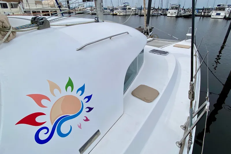 Slide: The Image of 2005 Lagoon 380 S2 catamaran with colorful sun design, docked at marina. - 13