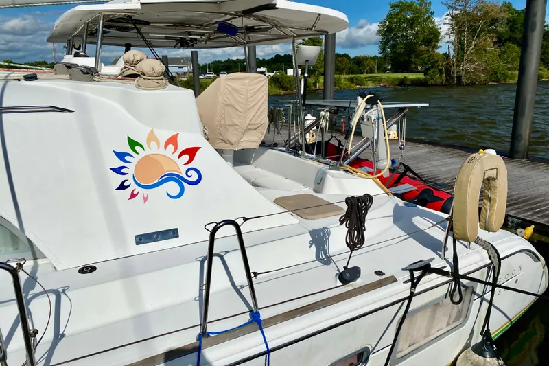 Slide: The Image of 2005 Lagoon 380 S2 catamaran docked, featuring colorful sun and wave design. - 6
