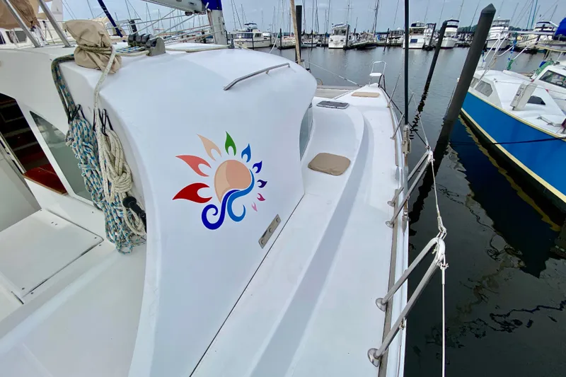 Slide: The Image of Catamaran Lagoon 380 S2, 2005 model, docked at marina with colorful logo on deck. - 12