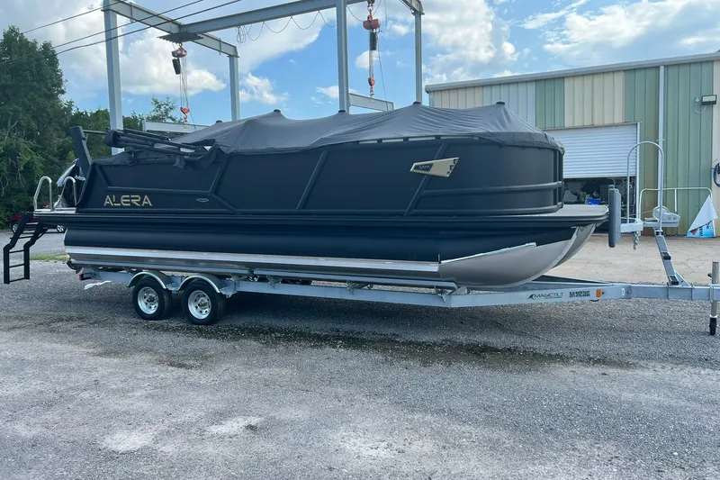 Slide: The Image of Alera M 23Q 2026 pontoon boat on trailer, covered and parked outdoors. - 0