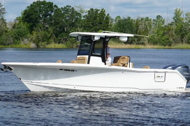 The Image of 2021 Sea Hunt Gamefish 27FS boat cruising on a calm river with lush greenery. - 1