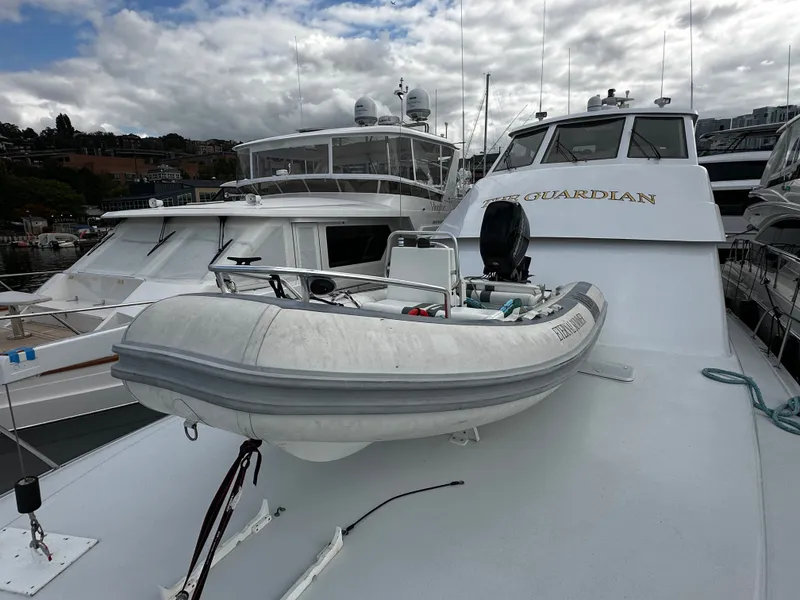 Slide: The Image of A 2000 Hatteras 70 Convertible with a small dinghy on deck, docked in a marina. - 47