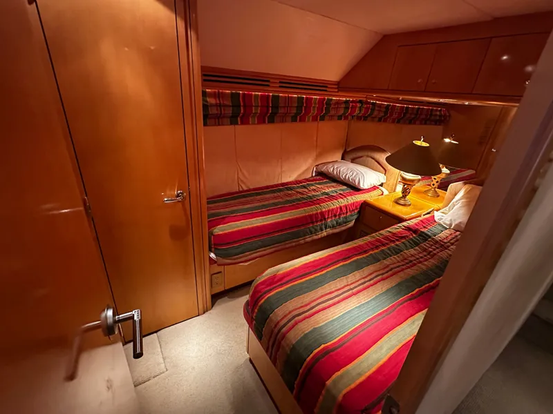 Slide: The Image of The cabin of the 2000 Hatteras 70 Convertible features two single beds with striped bedding. - 22