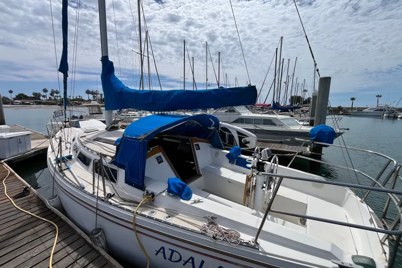 Slide: The Image of 1985 Catalina 30 sailboat docked at marina, featuring blue sail covers and clear skies. - 1