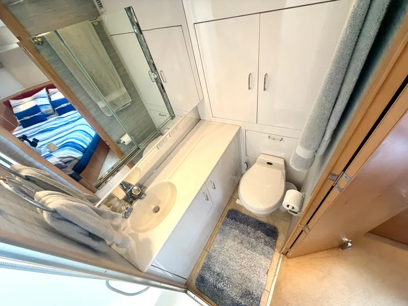 Slide: The Image of The image shows a yacht bathroom with a sink, toilet, and shower. A bedroom with striped bedding is visible in the background. - 24