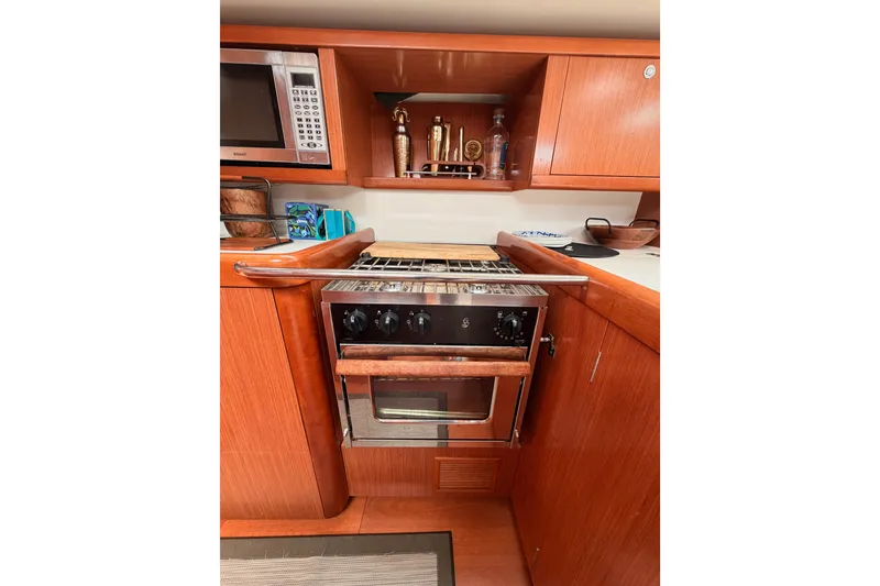 Slide: The Image of Galley kitchen in 2008 Beneteau 49 yacht with stove, microwave, and wooden cabinetry. - 48