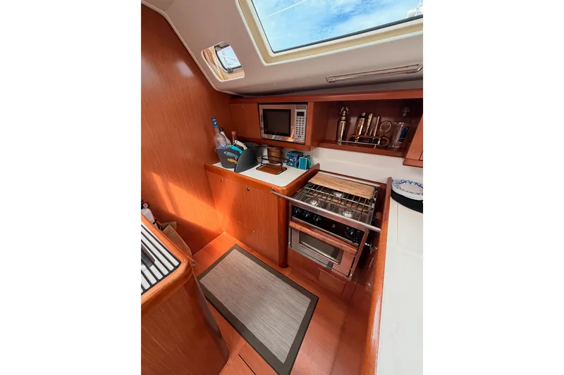Slide: The Image of Galley kitchen in 2008 Beneteau 49 yacht with stove, microwave, and wooden cabinetry. - 43
