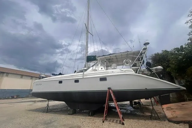 Slide: The Image of 2004 Manta 42 MkII catamaran on land, under cloudy sky, with support ladders. - 49