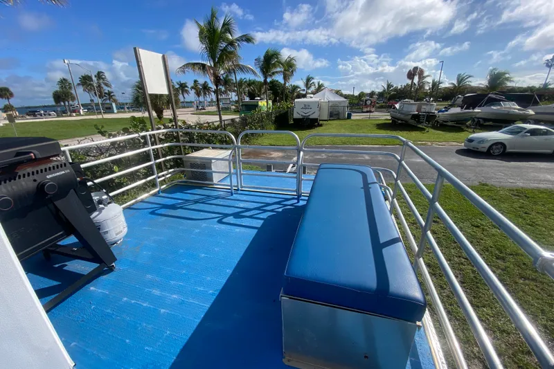 Slide: The Image of 2019 Solid Craft Commercial Pontoon with blue deck, bench seating, and grill, near palm trees. - 20
