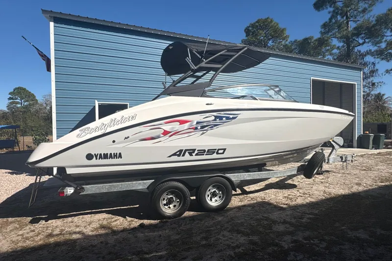 Slide: The Image of 2025 Yamaha Boats AR250 on trailer, parked outside blue building. - 0