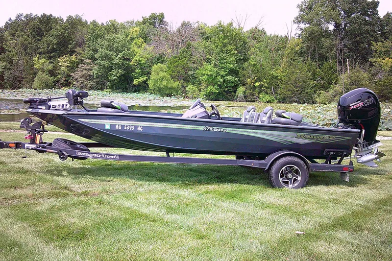 Slide: The Image of 2025 Ranger RT198P boat on trailer, parked on grass near a lake with trees. - 0