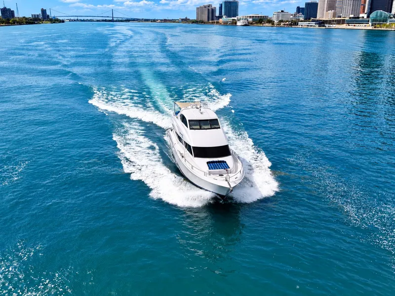 Slide: The Image of A 2002 Lazzara 80 Skylounge cruising on a wide river with a city skyline in the background. - 19