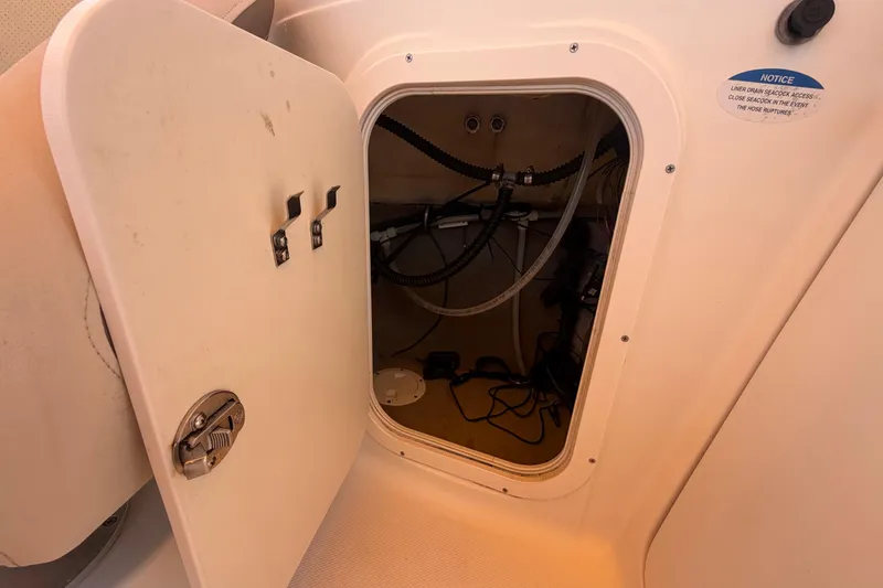 Slide: The Image of Open storage compartment on a 2006 Chaparral Sunesta 236 boat, showing internal wiring and hoses. - 41