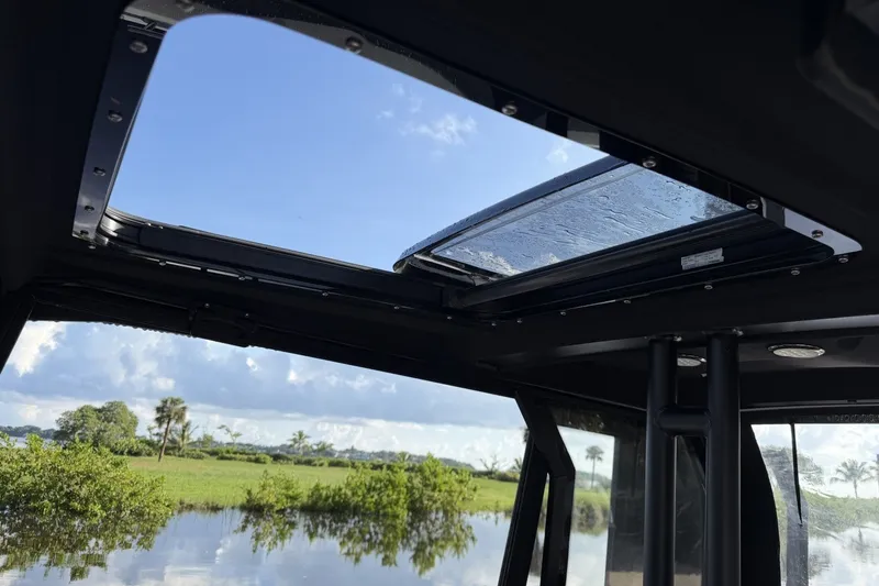 Slide: The Image of Open sunroof view from 2023 XO DFNDR 9 boat, overlooking lush greenery and water. - 9