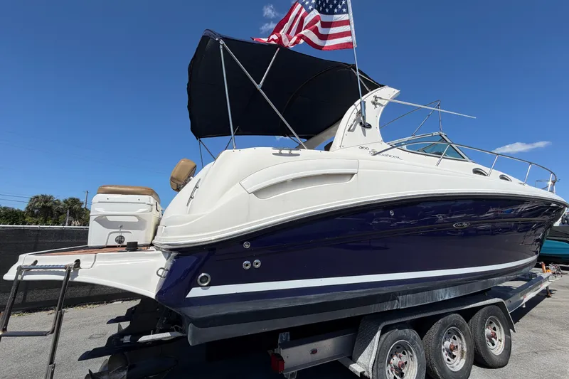 Slide: The Image of 2006 Sea Ray 300 Sundancer boat on trailer with American flag, under clear blue sky. - 2