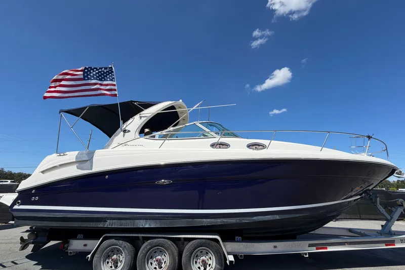 Slide: The Image of 2006 Sea Ray 300 Sundancer boat on trailer with American flag, under clear blue sky. - 1