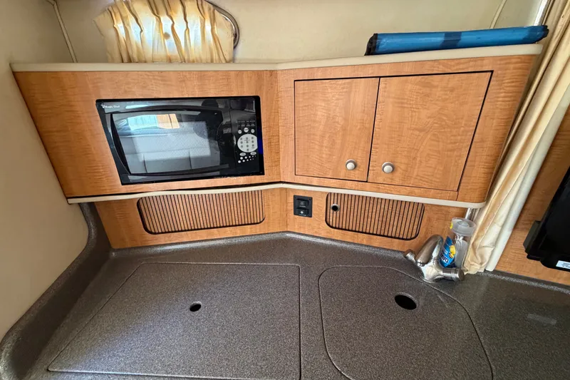Slide: The Image of 2006 Sea Ray 300 Sundancer kitchen with microwave, wooden cabinets, and countertop sink. - 67