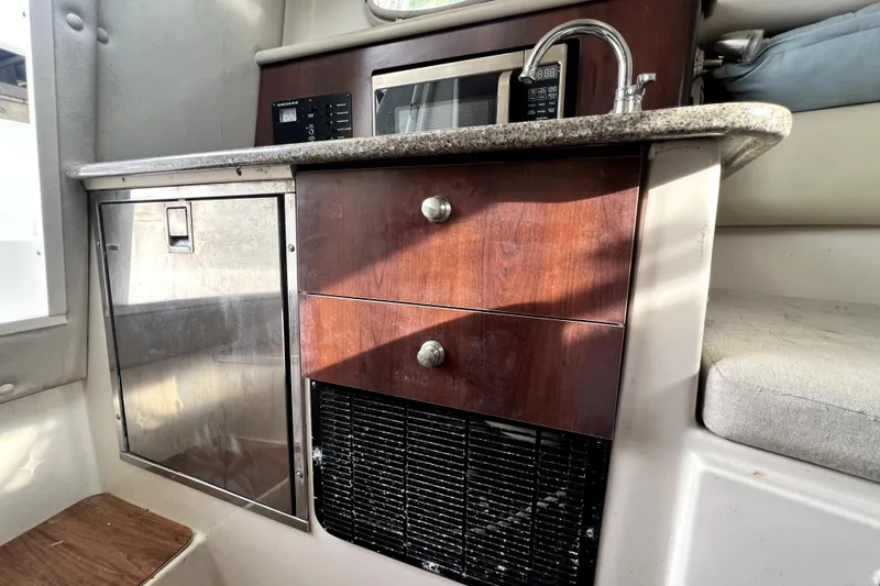Slide: The Image of 2014 Robalo R265 Walkaround cabin interior with kitchenette, featuring sink, microwave, and storage. - 128